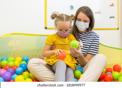 Toddler Girl In Child Occupational Therapy Session Doing Playful Exercises With Her Therapist During Covid - 19 Pandemic, Both Wearing Protective Face Masks.