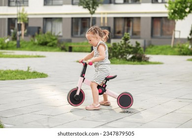 Toddler girl driving balance bike outdoors. Learning to ride bike concept. Urban.