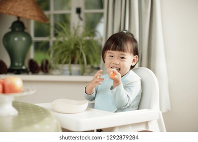 Toddler Girl Eating Yoghurt Sitting On High Chair Beside A Dinner Table At Home