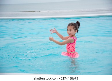 Toddler Girl Kid Swim Playful In Swimming Pool Summer Time With Pink Swimwear In Blue Water At Hotel Swimming Pool Outdoor. Happy Girl Swim Playful Water Splash With Happiness On Summer Vacation