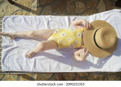 Toddler Girl Laying On Sun Bed And Hiding From Sun Under Straw Hat. Happy Summer Time Childhood Concept.