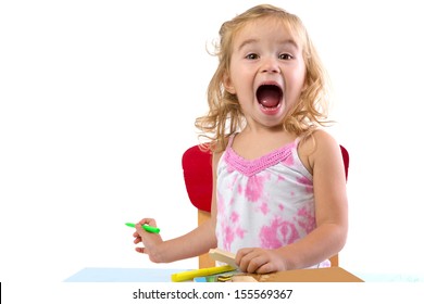 Toddler Girl Learning At The Table Very Excited , Her Eyebrowns Are Raised And Mouth Opened Large Holding Colorful Markers