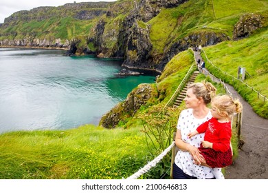 Toddler Girl And Mother On Carrick-a-Rede Rope Bridge, Famous Rope Bridge Near Ballintoy, Northern Ireland On Irish Coastline. Family Of Child And Woman On Bridge To Small Island On Cloudy Day.