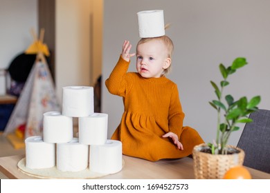 Toddler Girl Is Playing With Fullness Toilet Paper. Coronavirus Covid-19 Deficiency Rolls. Who Bought Up All Tissue Deficit . Panic. Meme Funny Baby