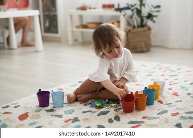 Toddler Girl Plays With Beads And Multicolored Buckets, The Development Of Fine Motor Skills And Sensory Development, The Study Of Colors. Self-study Of The Child And Montessori Method