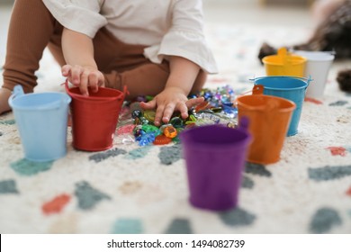 Toddler girl plays with beads and multicolored buckets, the development of fine motor skills and sensory development, the study of colors. Self-study of the child and Montessori method