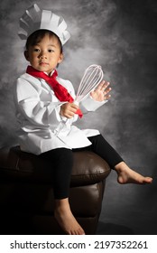 A Toddler Girl Portrait Is Holding A Whisk While Sitting On A Chair. 