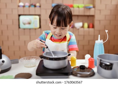 Toddler Girl Pretend Play Food Preparing Role Against Cardboard Blocks Kitchen Background