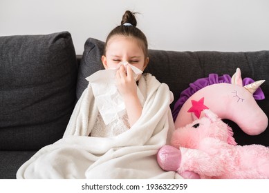 Toddler Girl Sits On The Couch And Blows Her Nose Into A Napkin. The Child Is Cold And Sick And Has A Runny Nose And Snot. Allergy, Flu