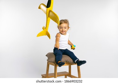 Toddler Girl Sits On Stool And Play Yellow Plane. Concept Of Gender Stereotypes.