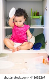 Toddler Girl Sitting In Kitchen Cupboard