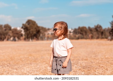 Toddler Girl Wear Casual T-shirt And Skirt Enjoy Sunny Day. Stylish Little Girl Walking In Field. Suburban Life, Unity With Nature