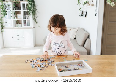 Toddler girl wearing pajamas playing puzzles at home. Stay at home activity for kids.