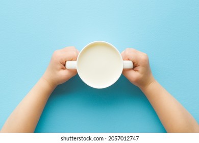 Toddler Hands Holding Cup Of White Fresh Milk On Light Blue Table Background. Pastel Color. Closeup. Point Of View Shot. Daily Healthy Drink.