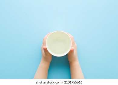 Toddler Hands Holding White Plastic Glass Of Fresh Water On Light Blue Table Background. Pastel Color. Closeup. Point Of View Shot. Daily Drink.