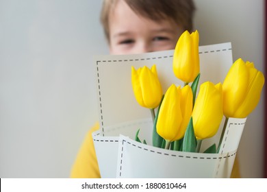 Toddler happy and smiling boy with a large bouquet of yellow tulips in Mothers Day. Portrait of a beautiful little kid on a gray background. Spring background