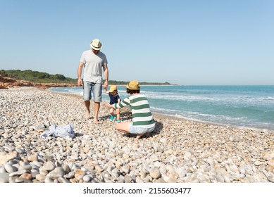 Toddler Holding Her Father Hand And Walking To Her Mom, Who Waits Her With Open Arms On A Mediterranean Beach. Summer Vibes.