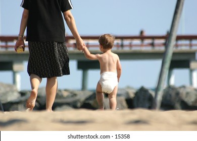 A toddler holds his mother's hand as he heads home from the beach.