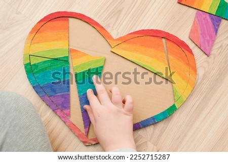toddler inserting piece of heart shape rainbow puzzle. table game. brain exercises at home. funny duck face, concentrated look. Montessori, fine motoric skills.
