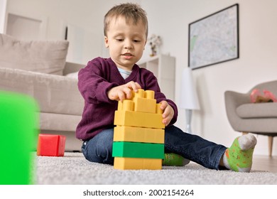 Toddler Kid Plays With Constructor At Home Sitting On Floor In Modern Living Room. Happy Child Building Creating Toy From Colorful Bricks. Early Education Classes For Preschoolers.