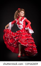 Toddler Little Girl Dancing Flamenco In Traditional Spanish Red Dress. Adorable Child From Andalusia With Curly Hair Dancing Gypsy Dance. Portrait Of Artist Baby In Carnival Bellydancing Costume