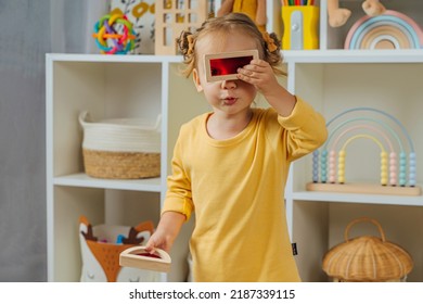 Toddler  Looking Through The Colorful Window Of A Toy. Educational Game For Baby  In Modern Nursery. A Little Girl Looking Through Transparent Colored Block Toy. Wooden Rainbow Stacking Blocks. 