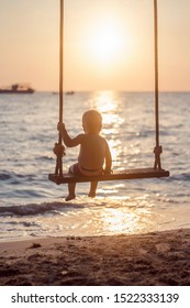 Toddler on a swing at sunset in the summer on the beach