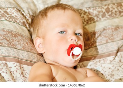 Toddler With Pacifier Lying On Bed