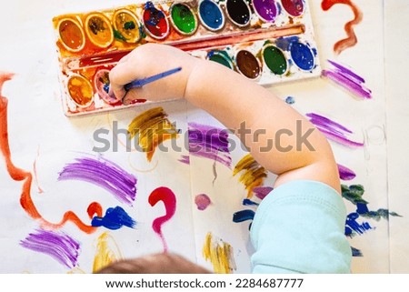 Toddler painting with paintbrush and colorful watercolor paints on white paper