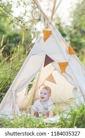 Toddler Playing In Cotton Teepee With Window, Decorated With Flags. One Year Cute Boy In A Teepee Outdoors.