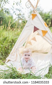 Toddler Playing In Cotton Teepee With Window, Decorated With Flags. One Year Cute Boy In A Teepee Outdoors.