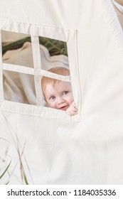 Toddler Playing In Cotton Teepee With Window, Decorated With Flags. One Year Cute Boy In A Teepee Outdoors.