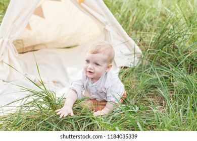 Toddler Playing In Cotton Teepee With Window, Decorated With Flags. One Year Cute Boy In A Teepee Outdoors.