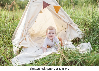 Toddler Playing In Cotton Teepee With Window, Decorated With Flags. One Year Cute Boy In A Teepee Outdoors.