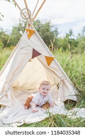 Toddler Playing In Cotton Teepee With Window, Decorated With Flags. One Year Cute Boy In A Teepee Outdoors.