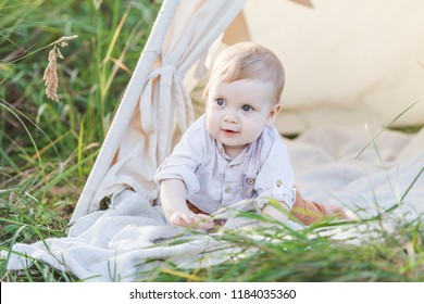 Toddler Playing In Cotton Teepee With Window, Decorated With Flags. One Year Cute Boy In A Teepee Outdoors.