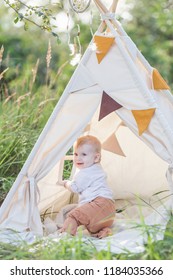 Toddler Playing In Cotton Teepee With Window, Decorated With Flags. One Year Cute Boy In A Teepee Outdoors.