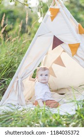 Toddler Playing In Cotton Teepee With Window, Decorated With Flags. One Year Cute Boy In A Teepee Outdoors.