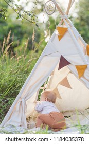 Toddler Playing In Cotton Teepee With Window, Decorated With Flags. One Year Cute Boy In A Teepee Outdoors.