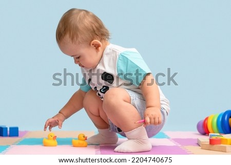 Toddler in the playroom grabs yellow rubber ducks for bathing from the floor.