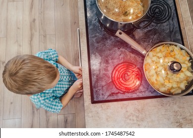 Toddler plays on kitchen with cooker for cooking. Child accident or burn. Unsafe home. Warning for curious children about dangers of handling stove. Hob scorching surface. Red hot cooktop