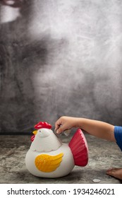 a toddler is putting a coin into a piggy bank in the shape of a chicken