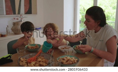 Toddler reaches for objects on table while mother intervenes and redirects behavior, expressing curiosity, disruption, and real life family interaction during mealtime