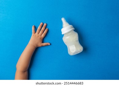 A toddler Reaching For milk feeding bottle, against blue back ground, top shot - Powered by Shutterstock