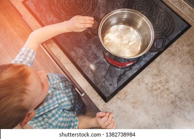 Toddler Reaching For Pan On The Stove. Child Safety Concept In Kitchen.