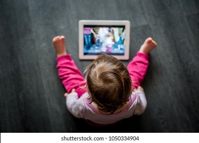 Toddler Sitting On The Floor Looking At Tablet Screen