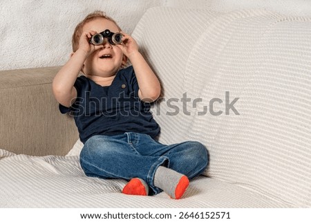 Toddler with tiny binoculars exploring his living room.
Amazed kid discovering his world more closely.