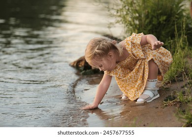 Toddler touching river water, fascinated by the ripples. Illustrates the purity of discovery and the first touch of nature. - Powered by Shutterstock