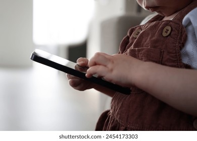 Toddler using smartphone indoors. Close-up of 15 month old child holding mobile phone and touching the screen. Photo taken in Sweden. - Powered by Shutterstock