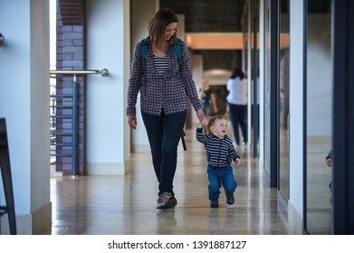 Toddler Walking In The Shopping Center With His Mom. Mother Takes The Son By The Hand